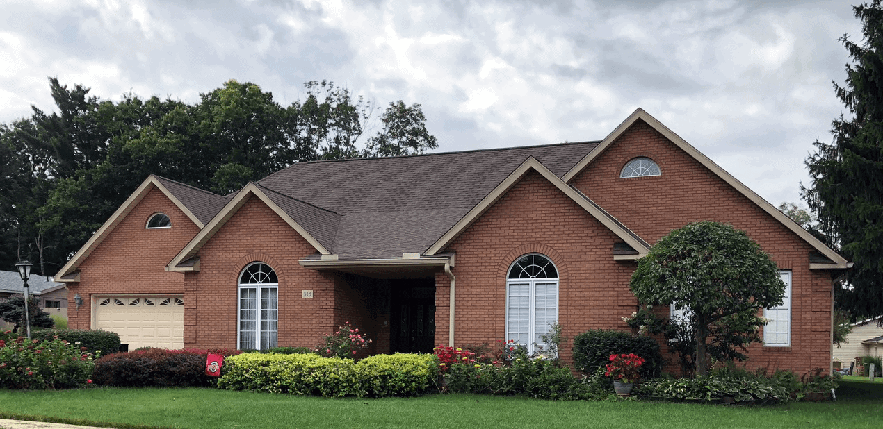 large brick home with flowers in front and asphalt shingle roof